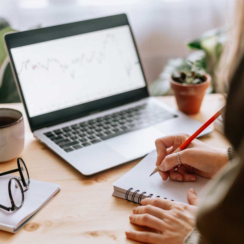 woman working at desk and taking written notes with laptop open